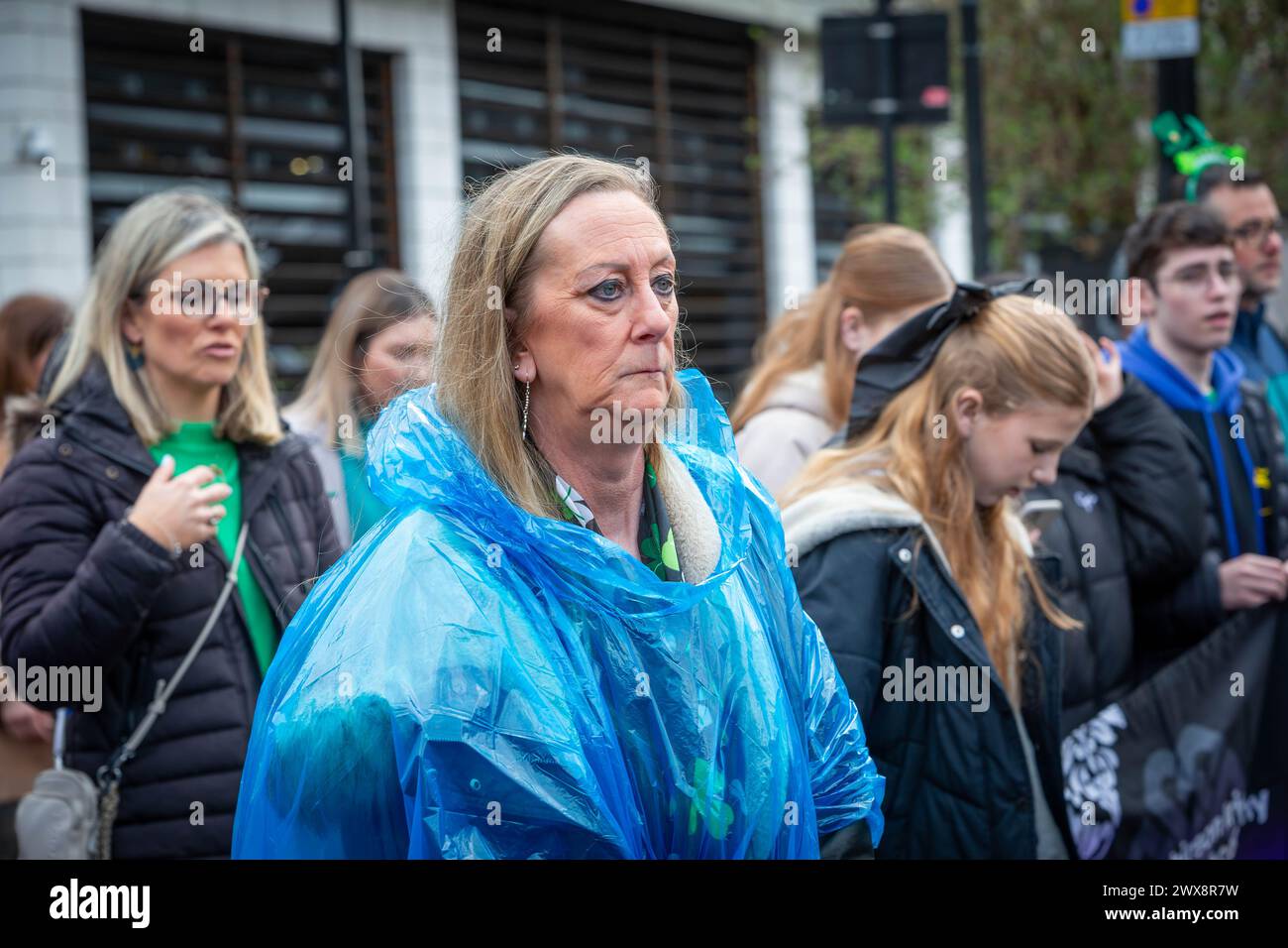 Unhappy lady in disposable poncho joins a procession in Warrington Town Centre for St Patrick's Day Stock Photo
