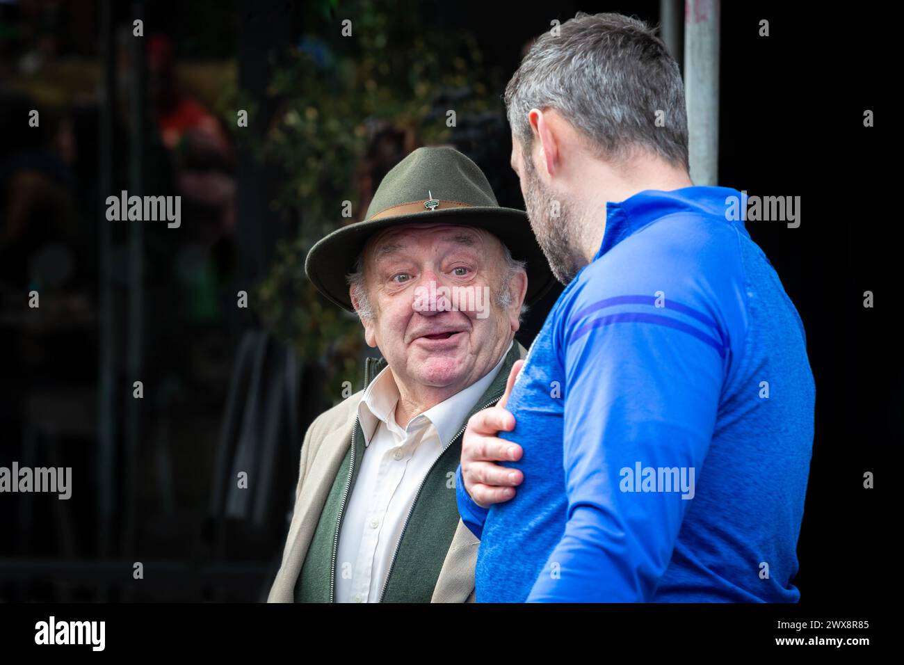 Man with Rhinophyma stands talking to a younger man in a blue top Stock Photo