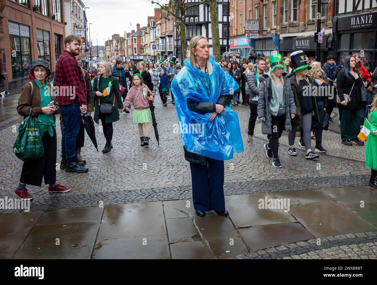 Unhappy lady in disposable poncho stands in the middle of a procession in Warrington Town Centre Stock Photo