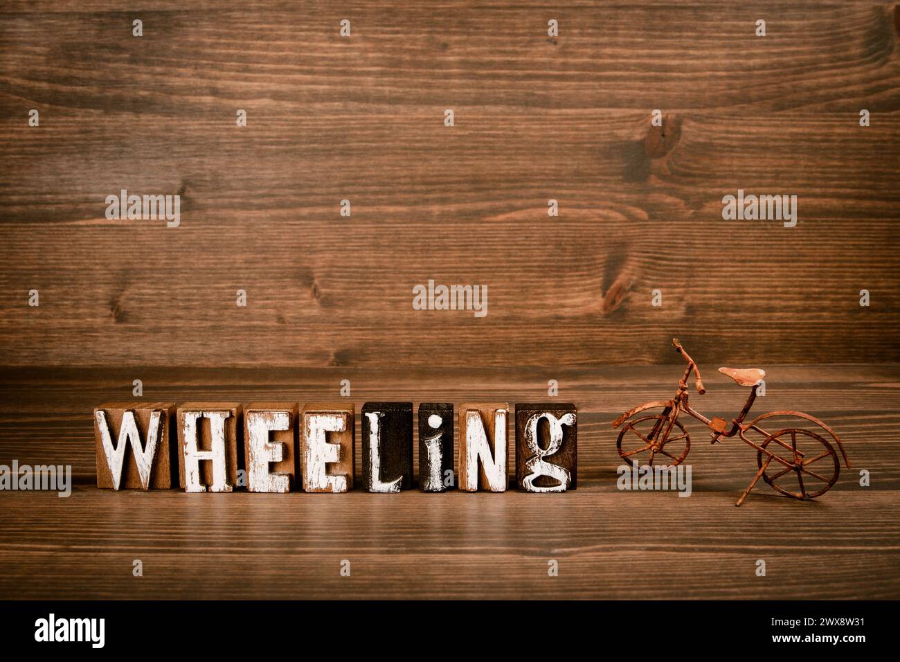 Wheeler Text WHEELING. Text from alphabet blocks and rusty miniature bicycle on wood ...