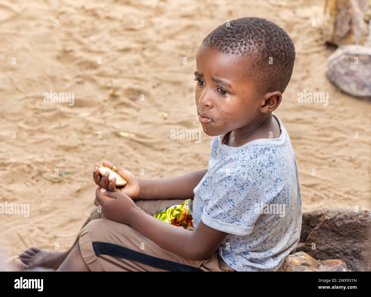 world famine , hungry african boy eating biscuits in the empty road, ngo social workers helping Stock Photo
