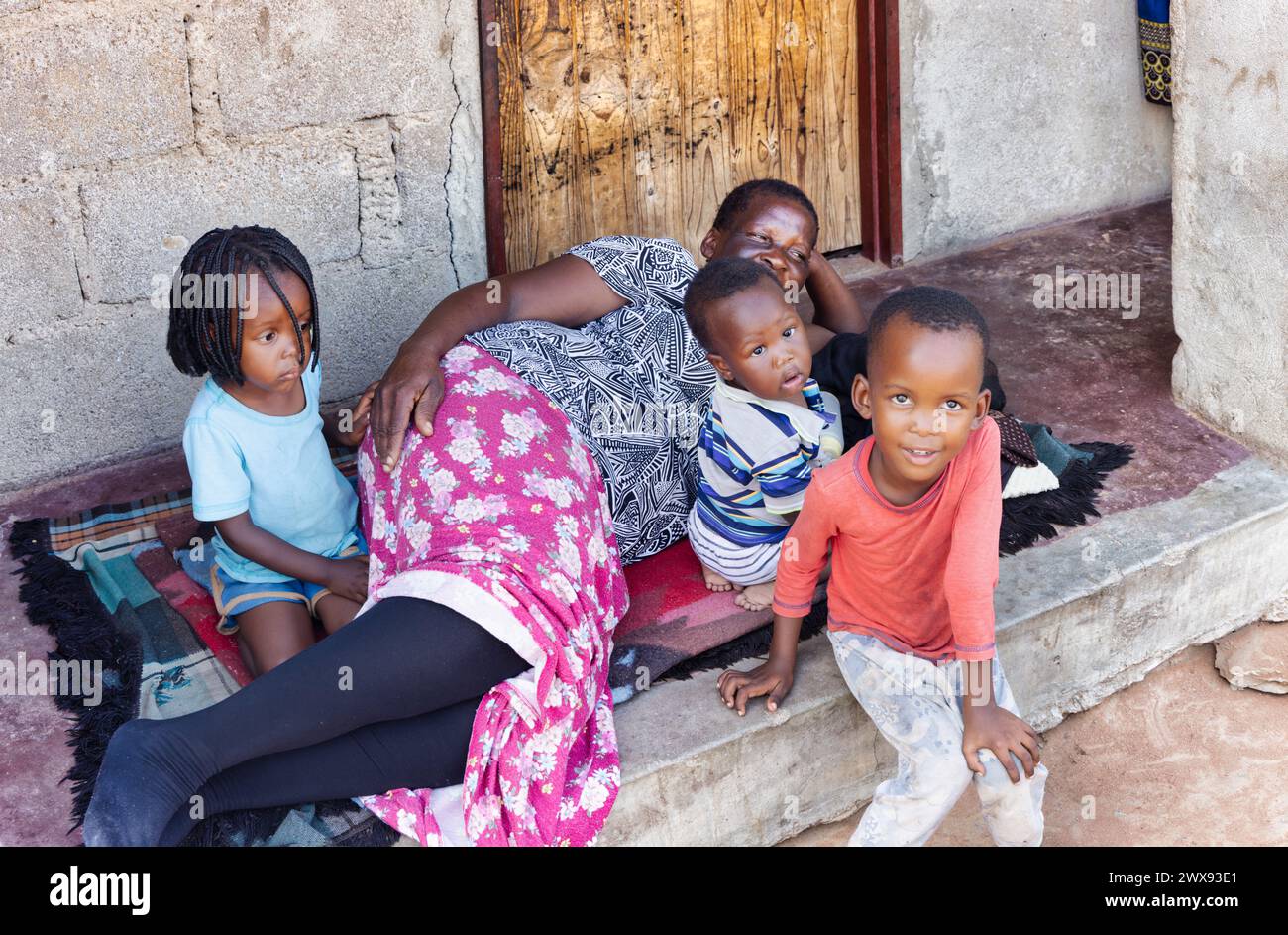 african old woman and grandchildren sited on the porch in front of the house, african village life Stock Photo