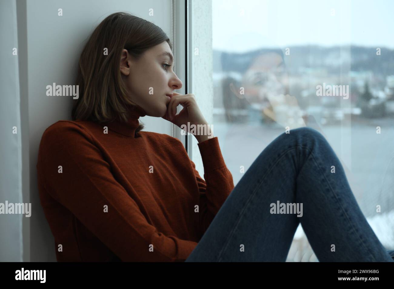 Sad young woman sitting on windowsill near window at home Stock Photo ...