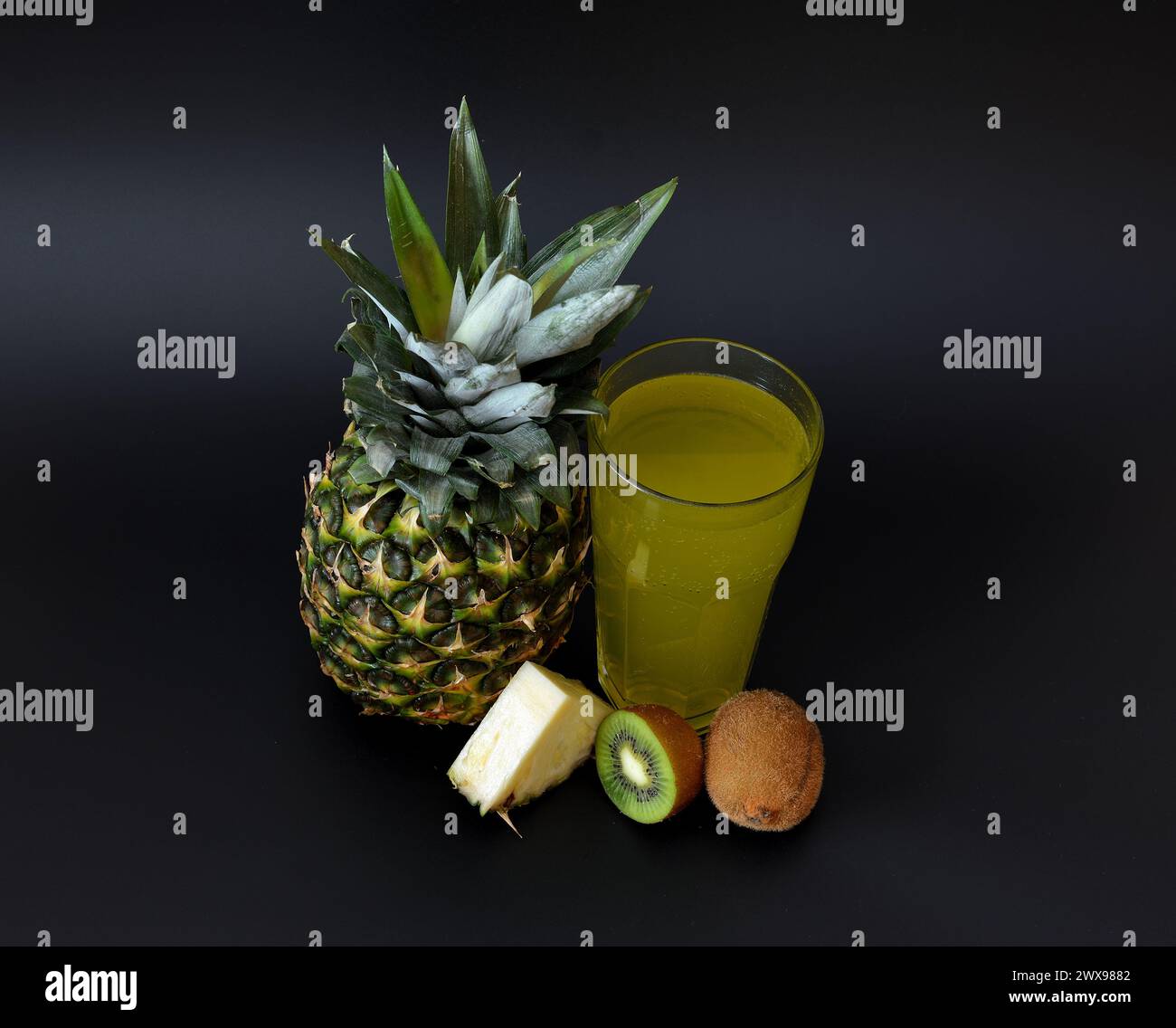Ripe pineapple, ripe kiwi slices and a glass of fresh fruit juice on a black background. Close-up. Stock Photo