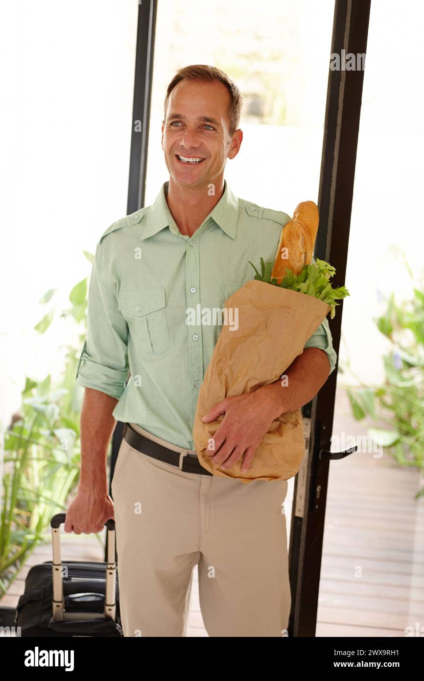 Smile, man and groceries bag in apartment with suitcase for work trip or holiday or vacation in California. Happy person, vegetables and bread as food Stock Photo