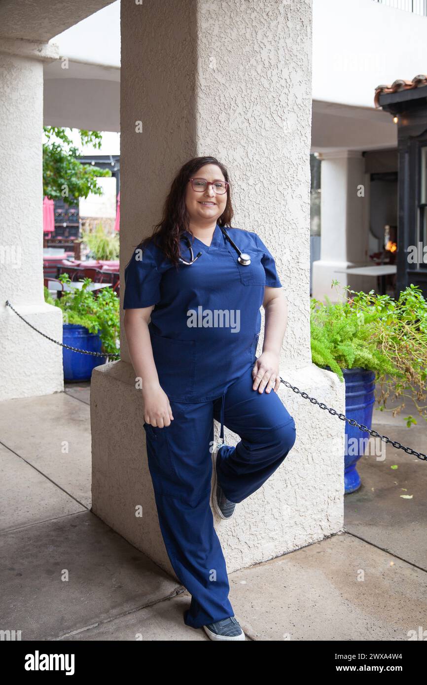 Young female nurse wearing blue scrubs standing outside Stock Photo