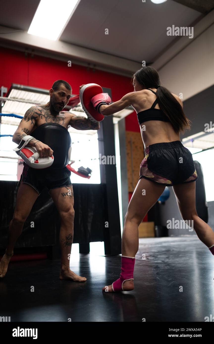 Strong female boxer practicing punching with trainer in gym Stock Photo