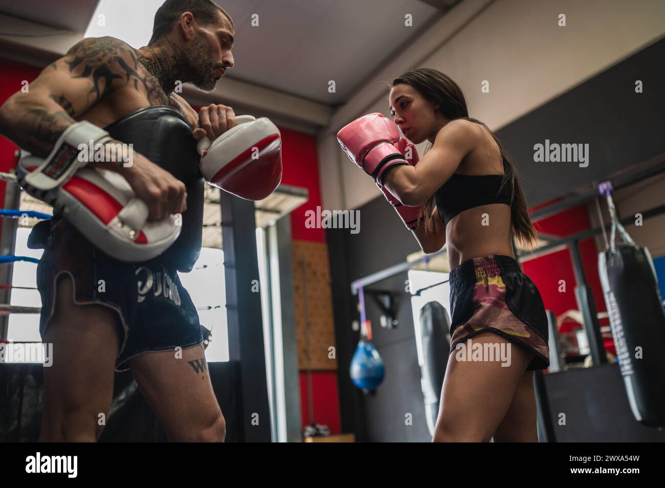 Strong female boxer practicing punching with trainer in gym Stock Photo