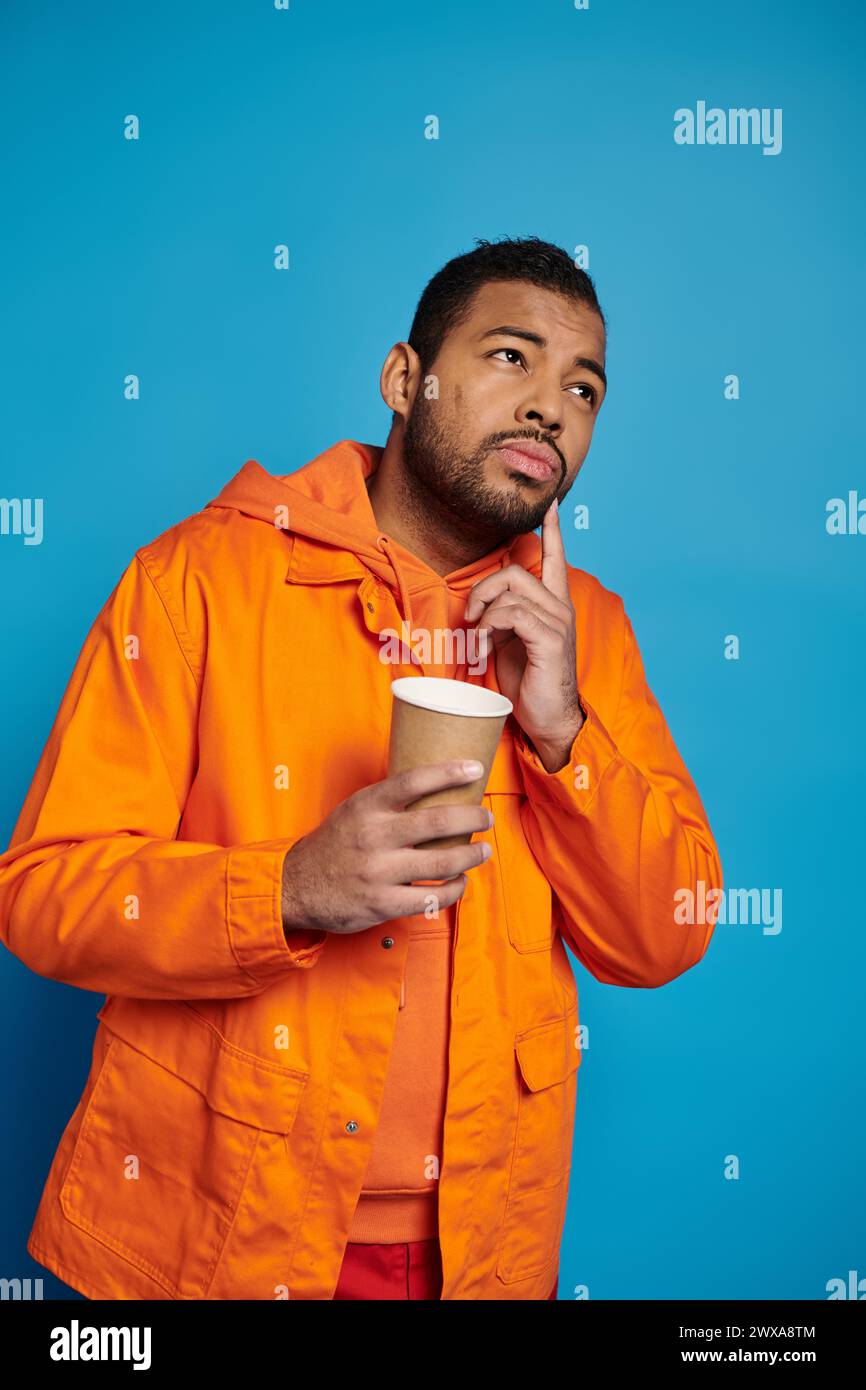 thoughtful african american man in his 20s with paper cup in hand on blue background Stock Photo