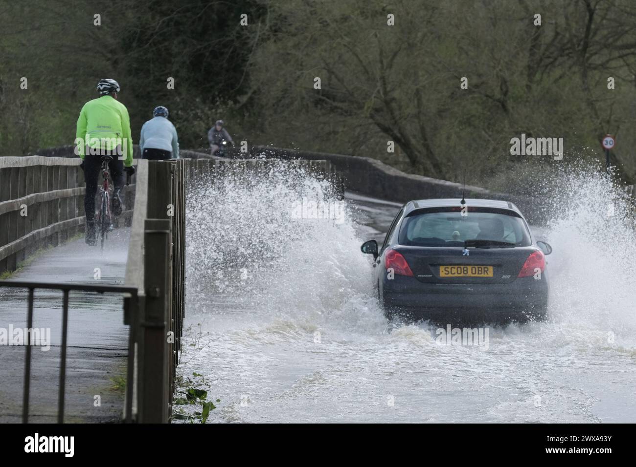 Lacock, Wiltshire, UK. 29th Mar, 2024. The River Avon in Lacock has burst its banks and flooded the road in and out of the village. Advice is not to drive through flood water but the road is passable if you want to make a splash. Credit: JMF News/Alamy Live News Stock Photo