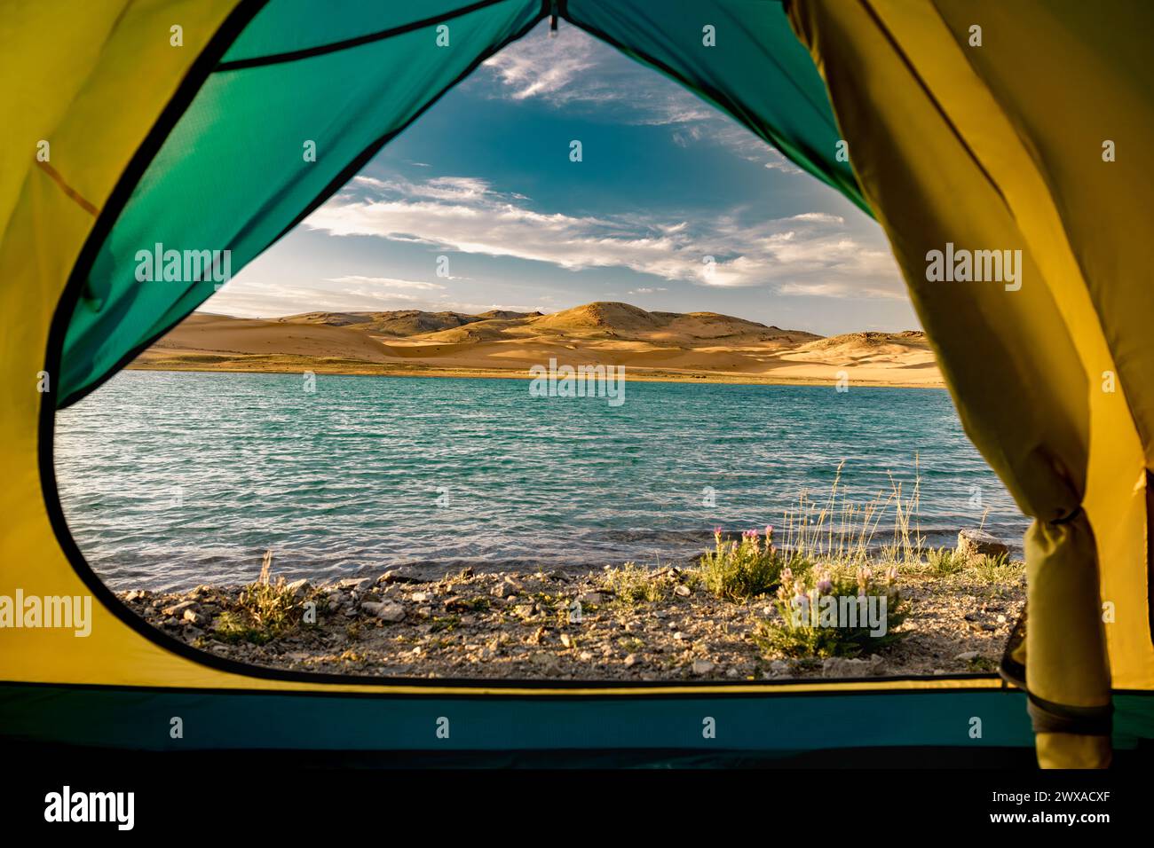 Nice view from tent at tranquil lake with turquoise water and sand dunes against blue sky Stock Photo
