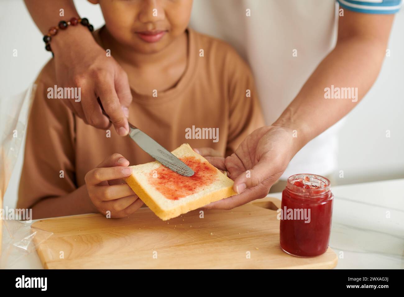 Father teaching son making breakfast sandwiches with strawberry jam Stock Photo