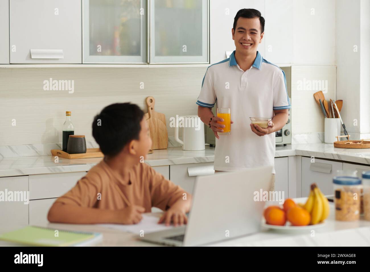 Smiling father bringing glass of juice and porridge to son doing ...