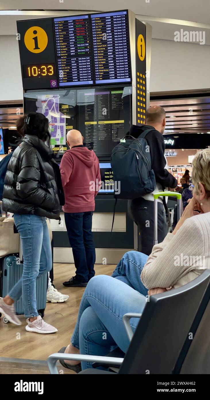 London,England: March 25.2024: Travelers checking the digital flight departure board for flight details at Heathrow airport in London,England Stock Photo