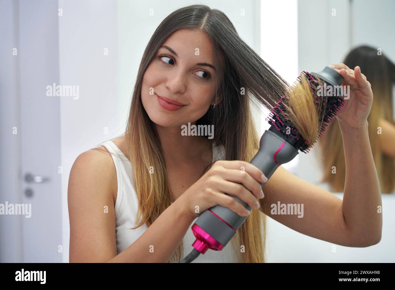 Hot air hair brush. Close-up of young woman using round brush hair dryer to style hair. Pretty girl using electric blowout brush hair dryer. Stock Photo