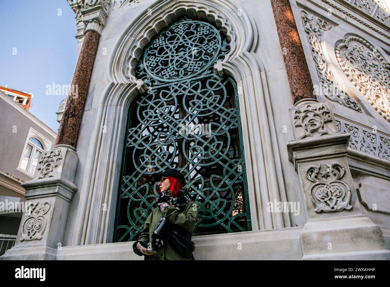 A person with a red headscarf looking through an intricate gothic window on a decorative stone facade Stock Photo