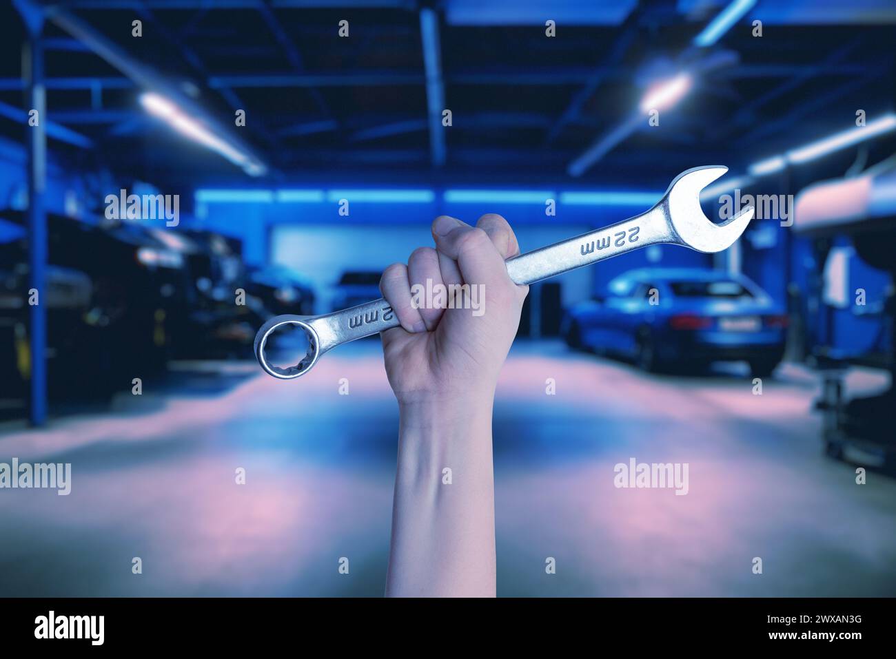 Wrench held in hand inside a car service garage. Illustrating the car service concept with automotive repair and maintenance Stock Photo