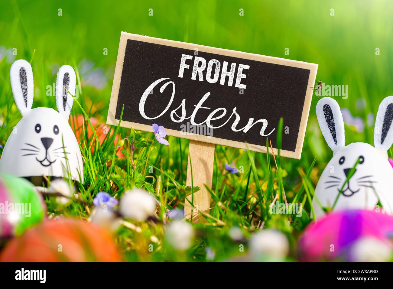 March 29, 2024: Easter eggs in a green meadow with bunny ears and a sign with the words: Happy Easter PHOTOMONTAGE *** Ostereier in einer grünen Wiese mit Hasenohren und einem Schild mit dem Schriftzug: Frohe Ostern FOTOMONTAGE Stock Photo