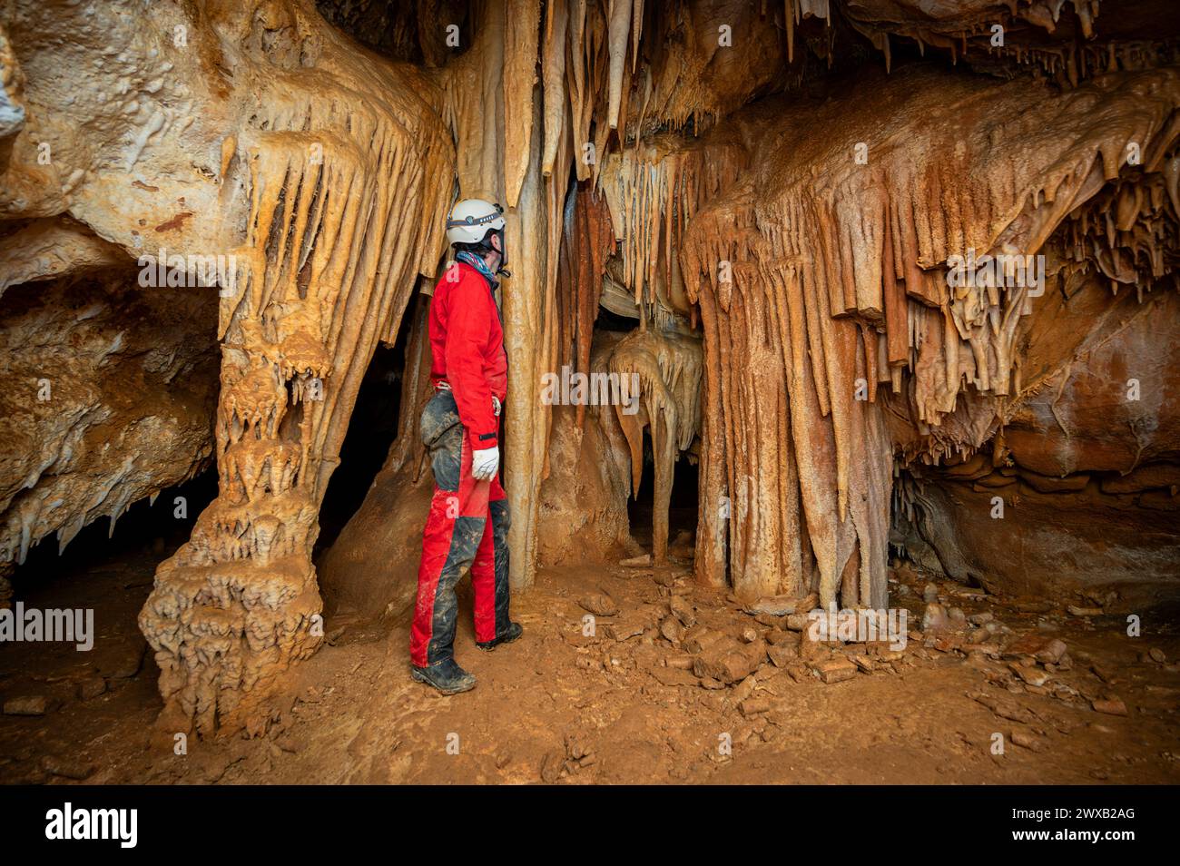 A speleologist with helmet and headlamp exploring a cave with rich ...