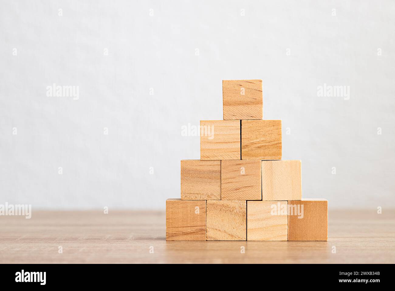 A neatly stacked pyramid of wooden blocks on a plain background. Stock Photo