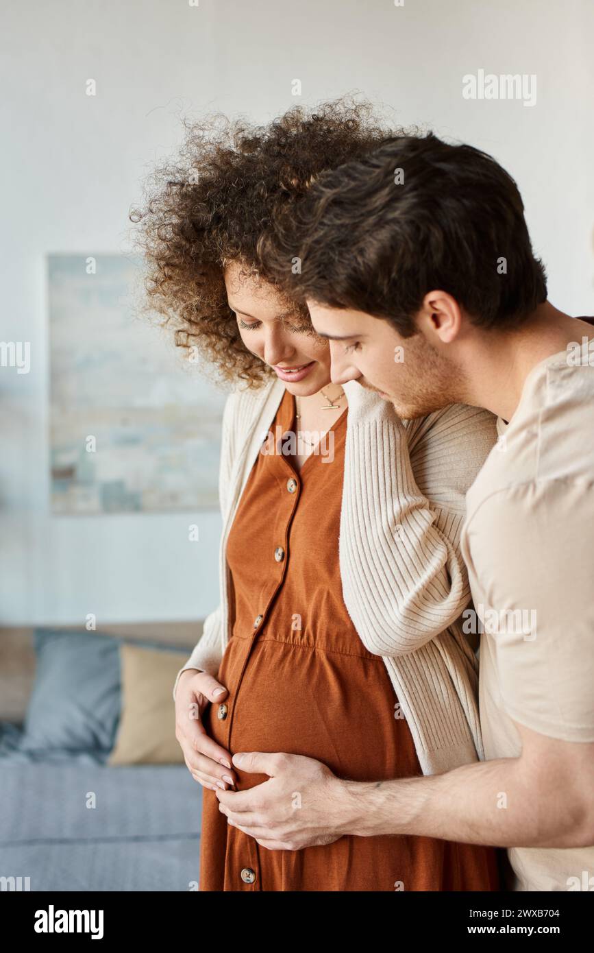 Lovely happy man hugging his pregnant wife from behind standing at home ...