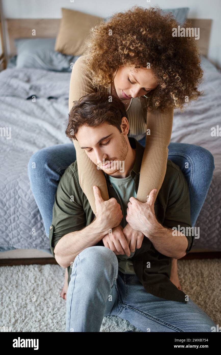 Lovely woman hugging her relaxed boyfriend from behind sitting on bed ...