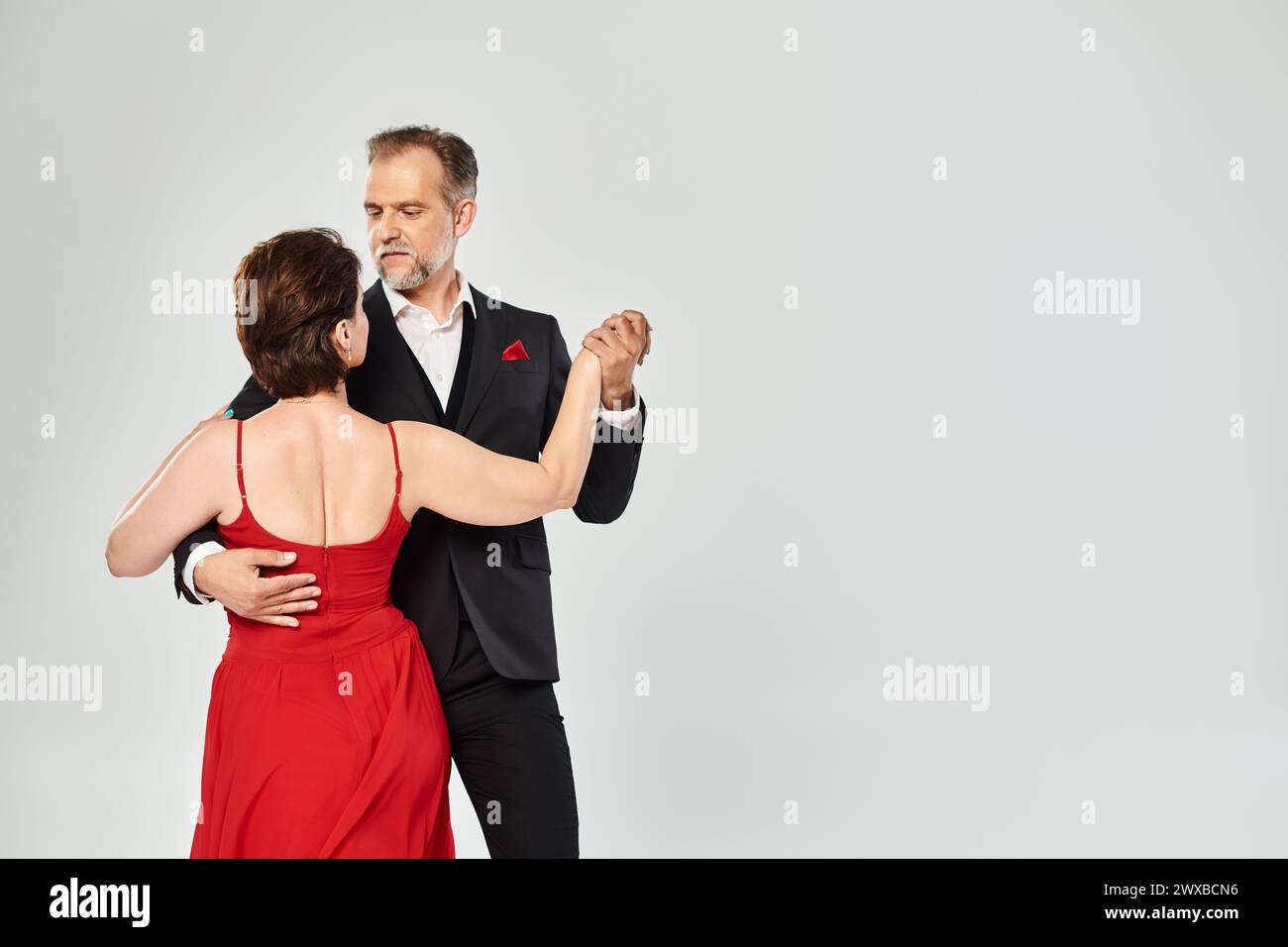 Middle aged attractive passionate couple dancing ballroom dance isolated on grey background Stock Photo