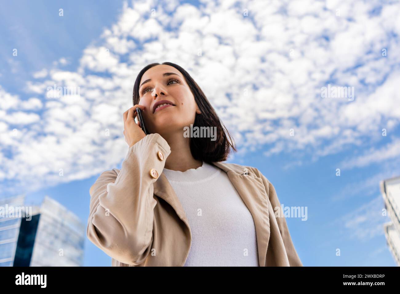 Low-angle view of a woman talking on her cell phone as she looks ahead Stock Photo