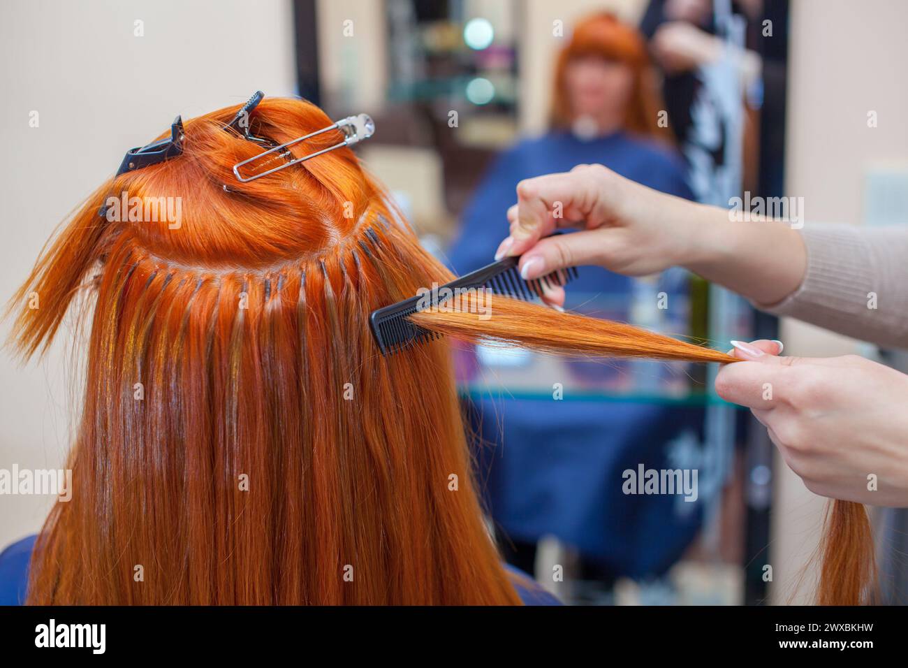 The hairdresser does hair extensions to a young, redhaired girl, in a