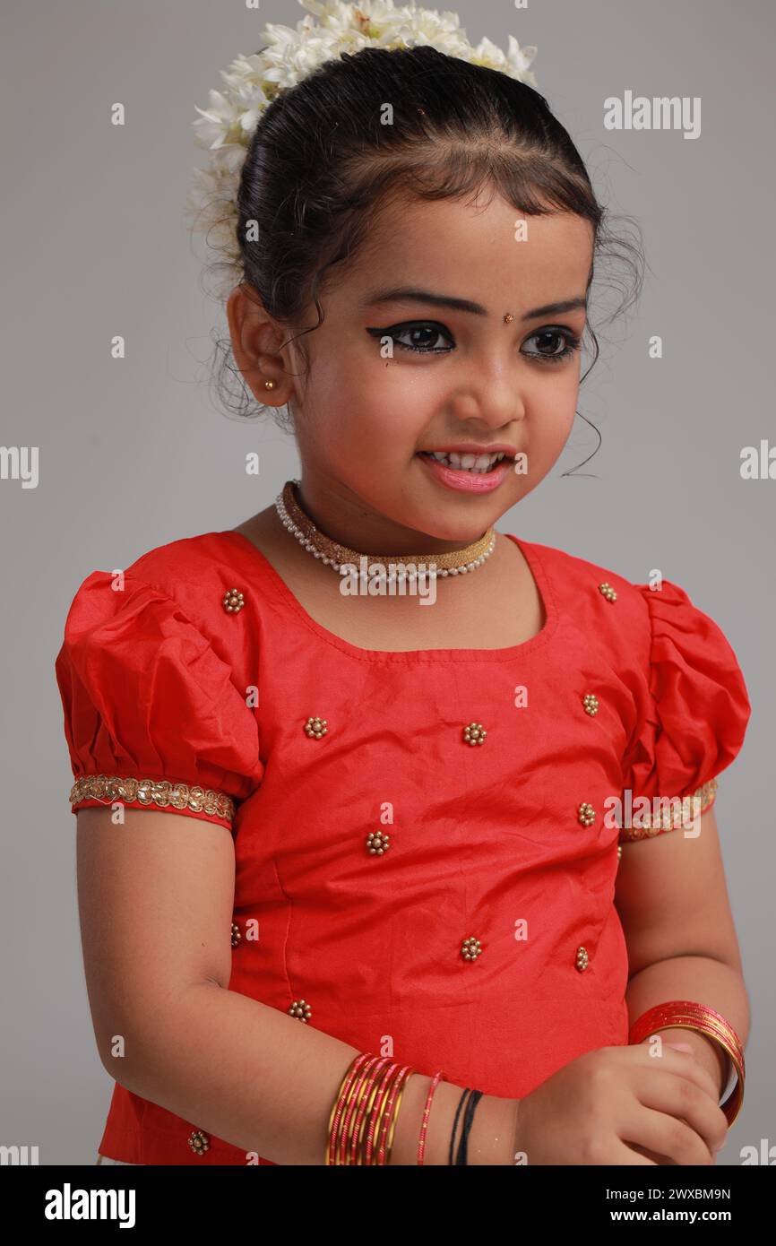 A cute small girl child wearing  Kerala dress-golden colour long skirt and red blouse with golden shower flower ,isolated Stock Photo