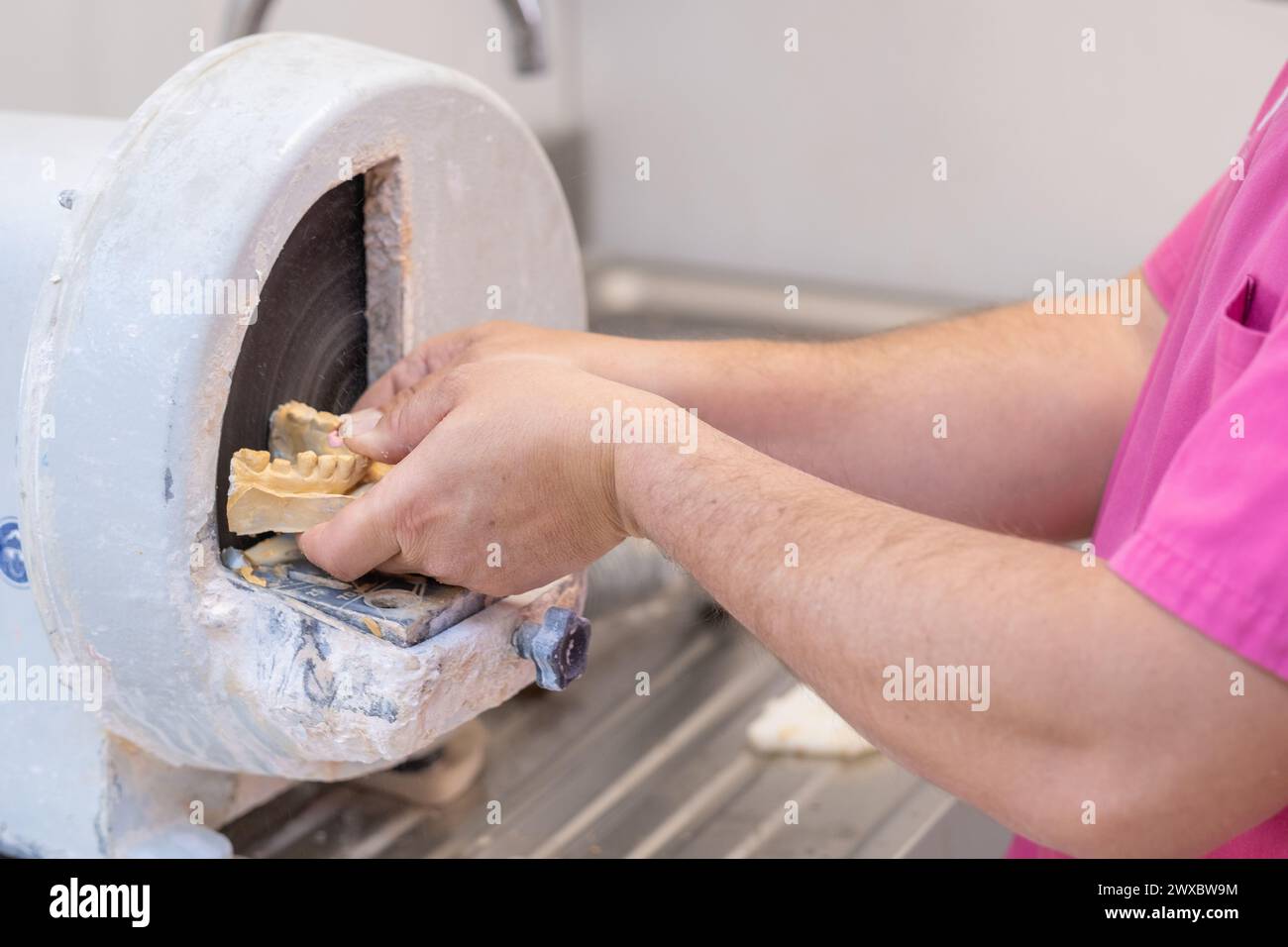 A dental technician levels a piece of dental stone with the trimmer or disc sander to make it ready to work on. Stock Photo