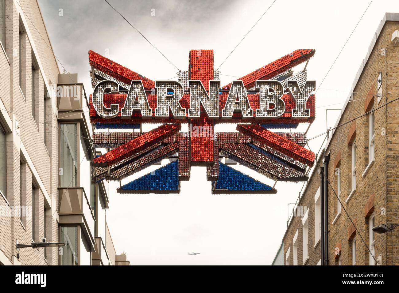 The shimmering Union flag above Carnaby Street is a symbol of British culture and fashion, it's mirror discs reflecting the area's vibrant atmosphere. Stock Photo