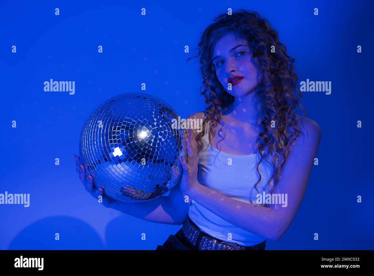 Woman looks absolutely stunning as she poses with disco ball in nightclub. Blue neon lights add touch of sensuality to scene Stock Photo