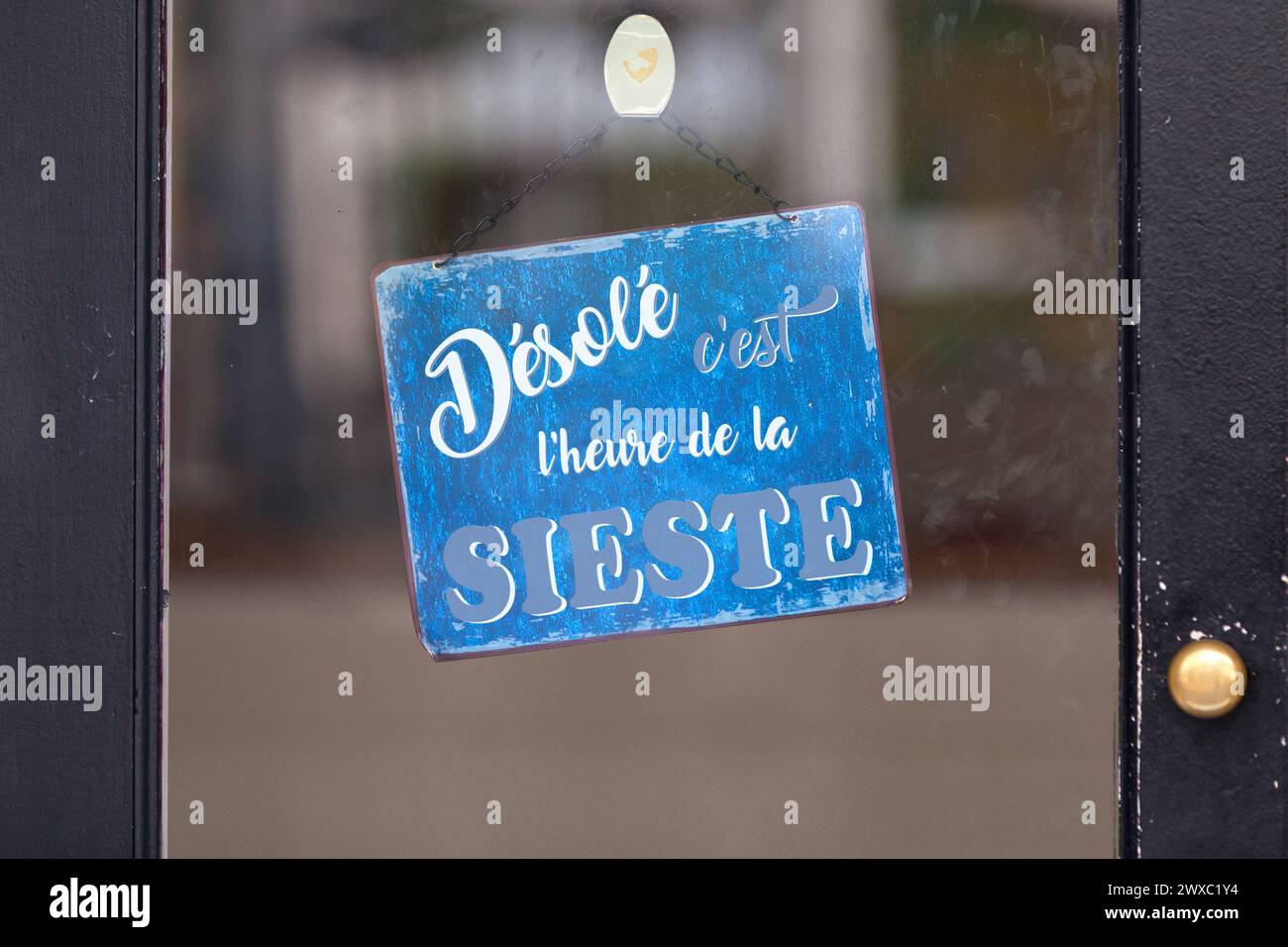 Blue open sign with written in it in French 'Désolé, c'est l'heure de la sieste', meaning in English 'Sorry, it's naptime'. Stock Photo