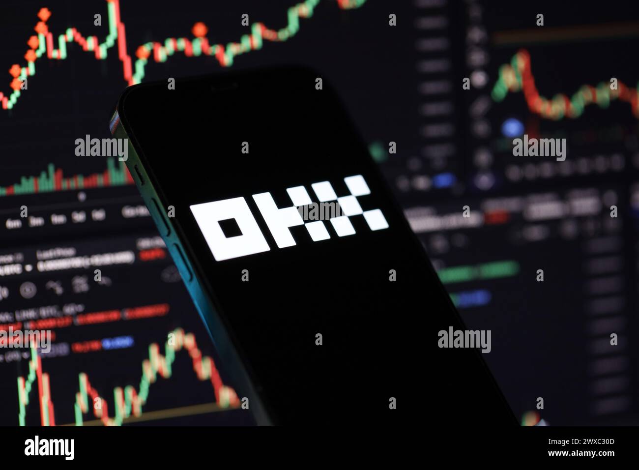 KYIV, UKRAINE - MARCH 15, 2024 OKX logo on iPhone display screen and crypto currency value charts. Cryptocurrency exchange portal Stock Photo
