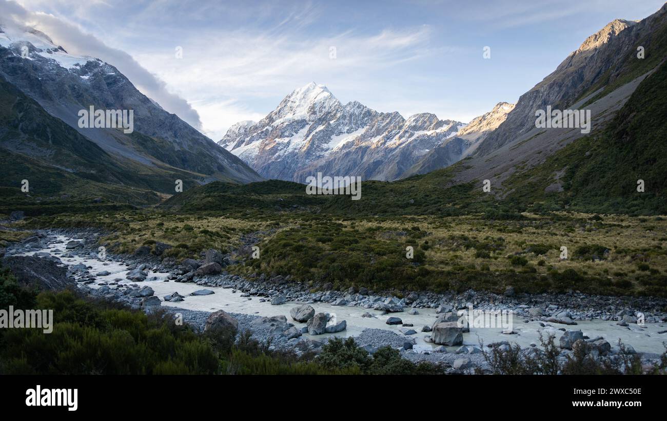 Scenic alpine valley with glacial river flowing through and prominent peak in backdrop during sunset. Stock Photo