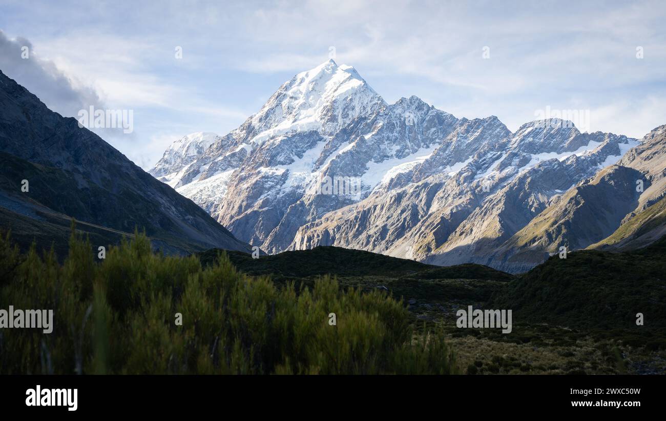 Massive snowy mountain with glacier catching the last light and towering above shaded alpine valley. Stock Photo