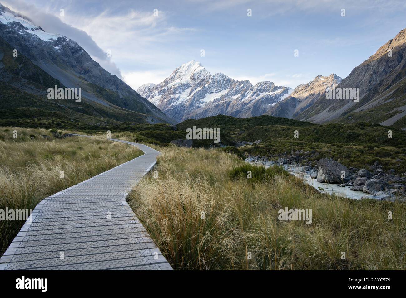 Wooden boardwalk leading through beautiful alpine valley with snowy mountain in backdrop,New Zealand. Stock Photo