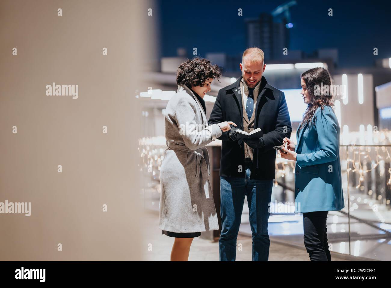 Three people sharing ideas on digital tablet at evening business event. Stock Photo