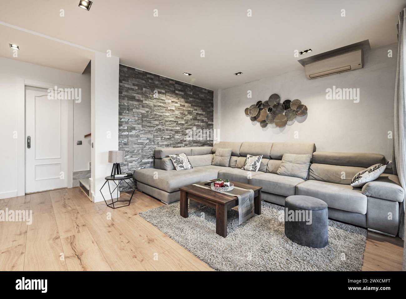 Living room with coffee table and corner sofa upholstered in gray fabric, shaggy rug and decorative slate brick wall Stock Photo