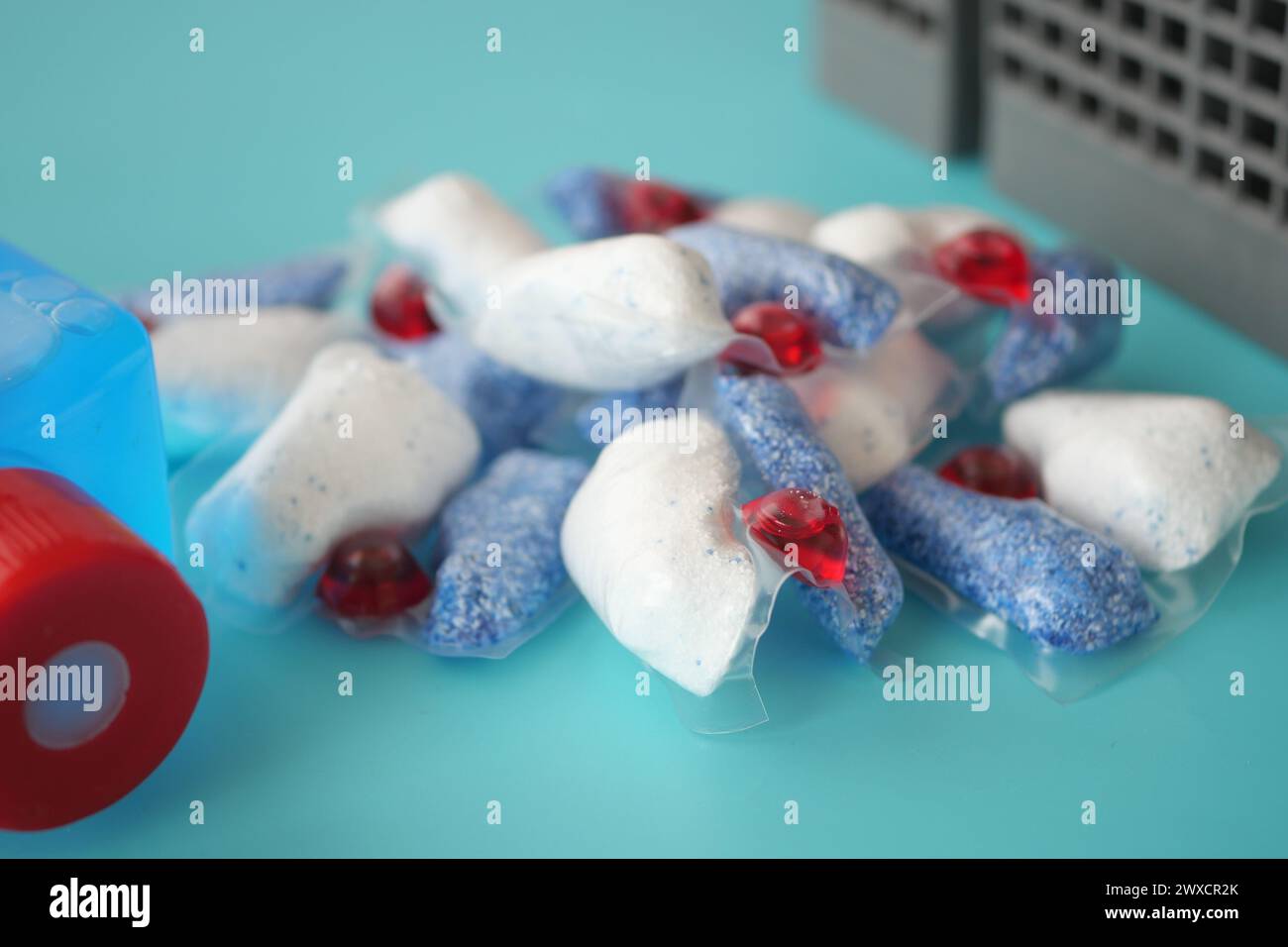 A stack of dishwasher tablets and a bottle of detergent on a blue background Stock Photo