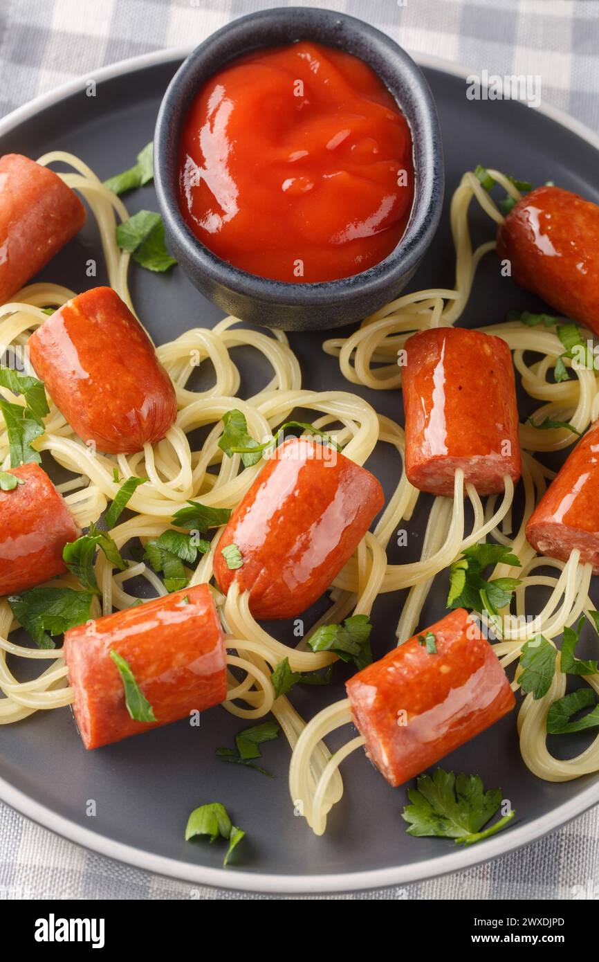 Delicious spaghetti hot dog in the form of spiders and ketchup close-up in a plate on the table. Vertical top view from above Stock Photo