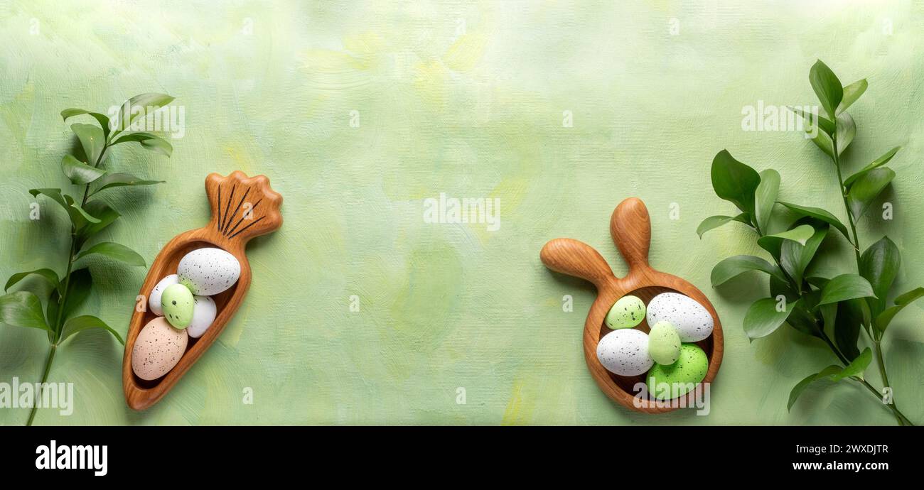 Easter wooden figured plates in form of bunny and carrot with decorative Easter eggs and green Ruskus twigs on textured green yellow background. Creat Stock Photo
