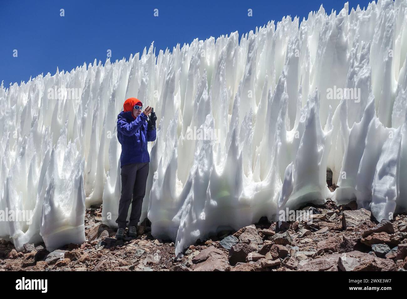 Woman in Atacama Desert near Ojos del Salado, in Chile, captures penitentes with her camera. The ice formations create a unique and surreal landscape. Stock Photo