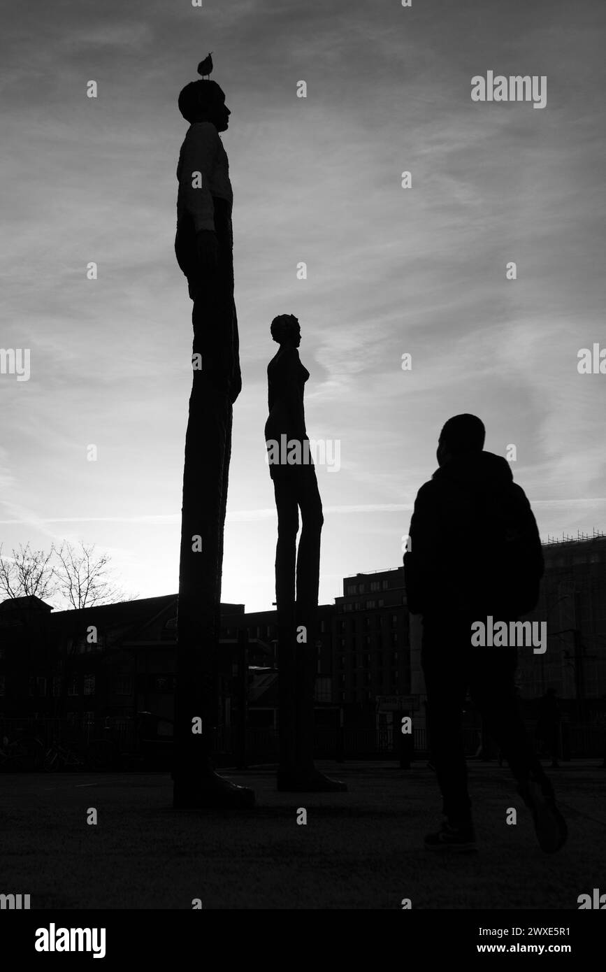 Where Art Meets Life - A pedestrian's silhouette intertwines with the enduring figures of public sculptures at dusk Stock Photo