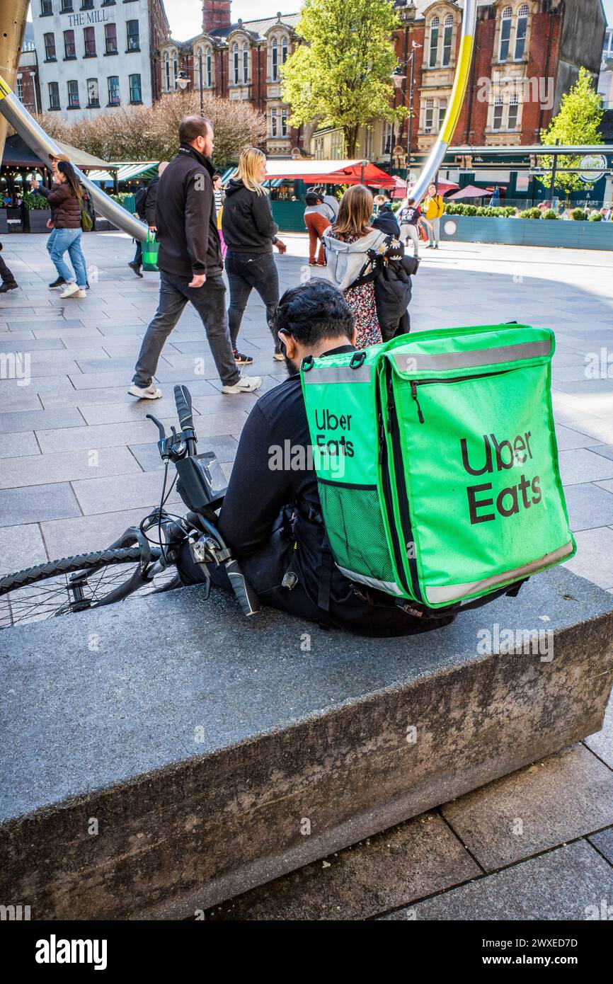 A deliver driver for Uber Eats (UberEats) sits with  his bike (bicycle). Illustration of Uber home food delivery platforms, in Cardiff, UK Stock Photo