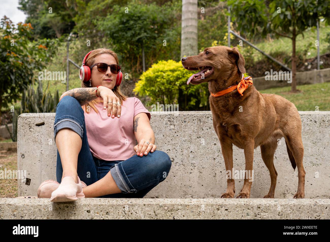 A tranquil woman with headphones sits in the plaza accompanied by her faithful pet. Stock Photo