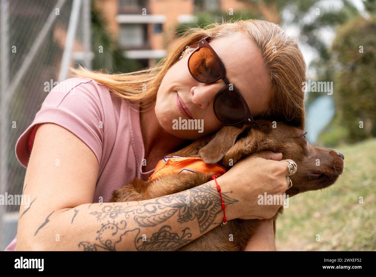 Close-up of a woman with closed eyes and sunglasses hugging her dog affectionately. Stock Photo