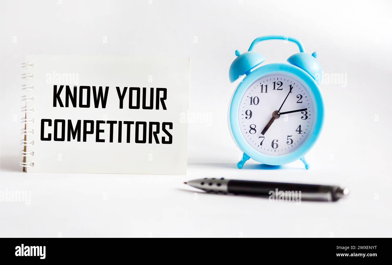 Office desk with clock, pen and notepad with text KNOW YOUR COMPETITORS Stock Photo