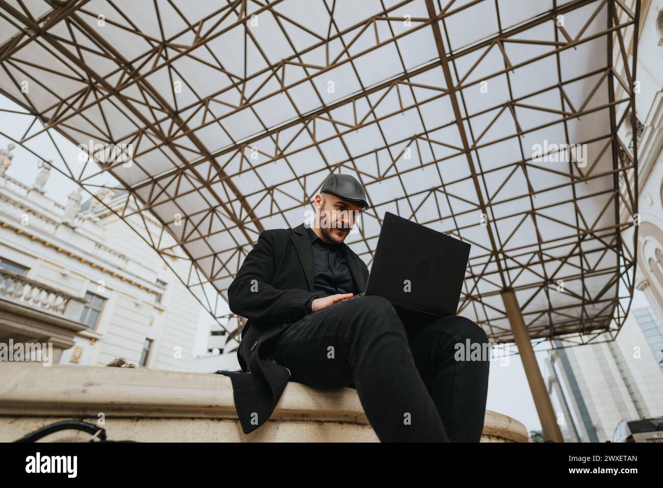 Stylish young man with laptop working outdoors under geometric canopy ...